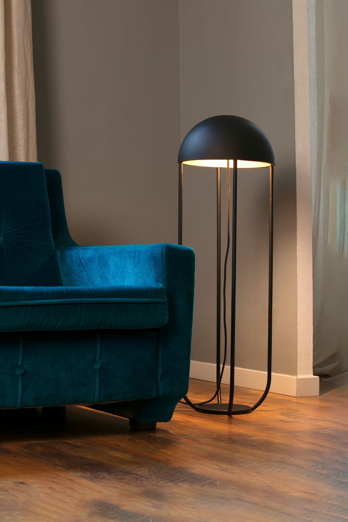 Modern floor lamp next to a blue sofa in a room with wooden flooring and neutral walls.