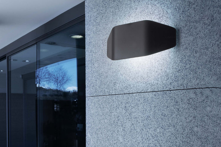 Modern black cylindrical outdoor ceiling light illuminating a stone facade