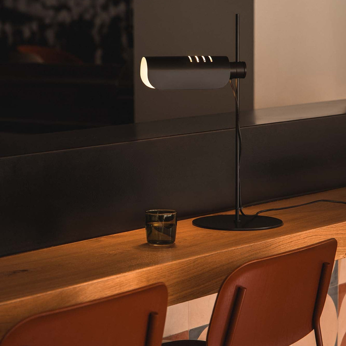 Modern lamp on a wooden table with two chairs in a dimly lit room.