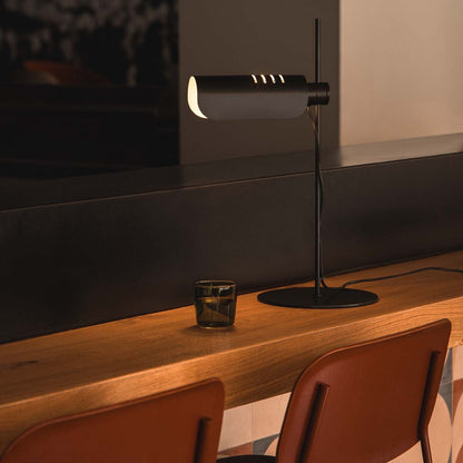 Modern lamp on a wooden table with two chairs in a dimly lit room.