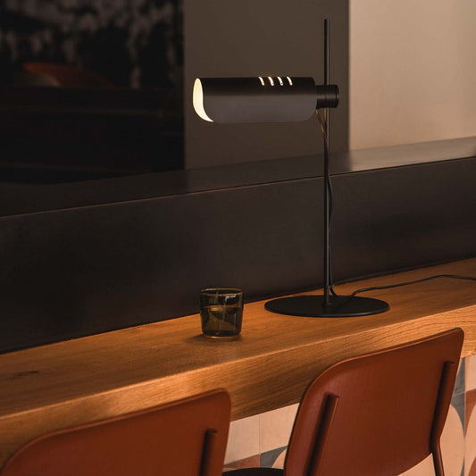 Modern lamp on a wooden table with two chairs in a dimly lit room.