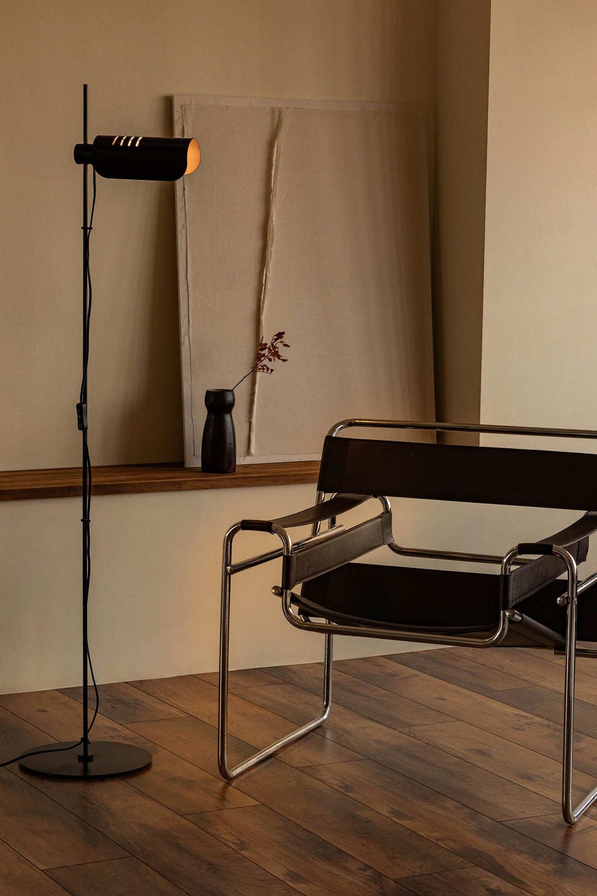 Modern chair and floor lamp in a minimalistic room with wooden flooring and neutral walls.