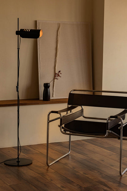 Modern chair and floor lamp in a minimalistic room with wooden flooring and neutral walls.