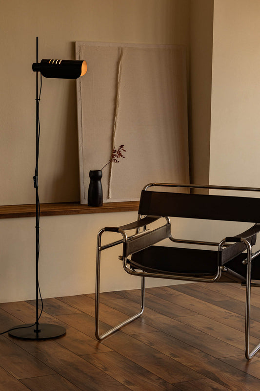 Modern chair and floor lamp in a minimalistic room with wooden flooring and neutral walls.