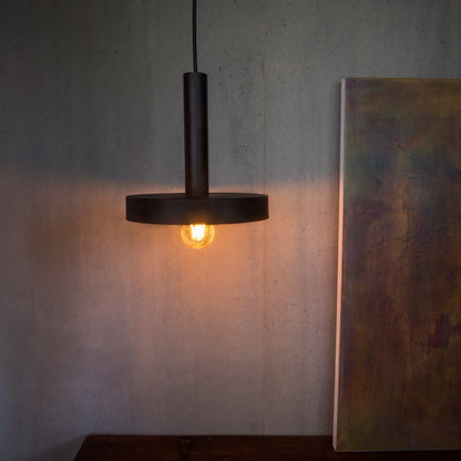 Dark pendant light hanging above a wooden surface with a neutral wall background