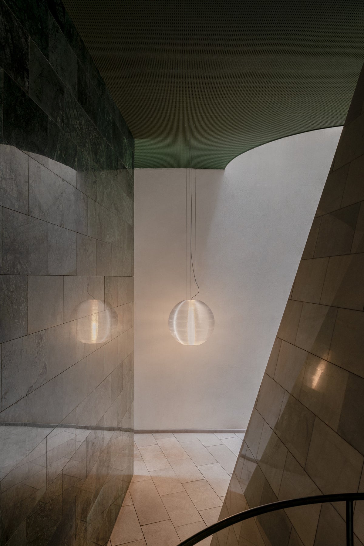 Modern pendant light fixture in a minimalistic interior setting with curved walls.