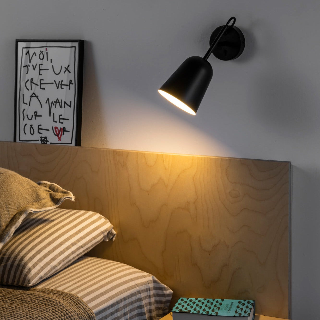 Modern bedroom with wooden headboard, black wall lamp, and framed artwork.