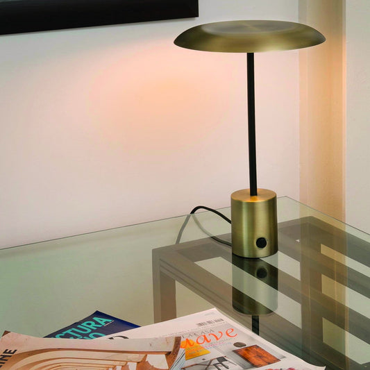 Gold table lamp on a glass surface with a cityscape painting in the background