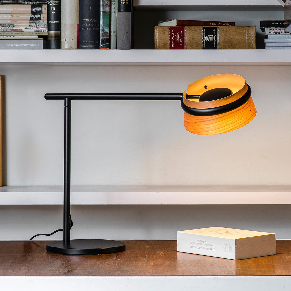 Modern desk lamp on a wooden surface with books on shelves in the background