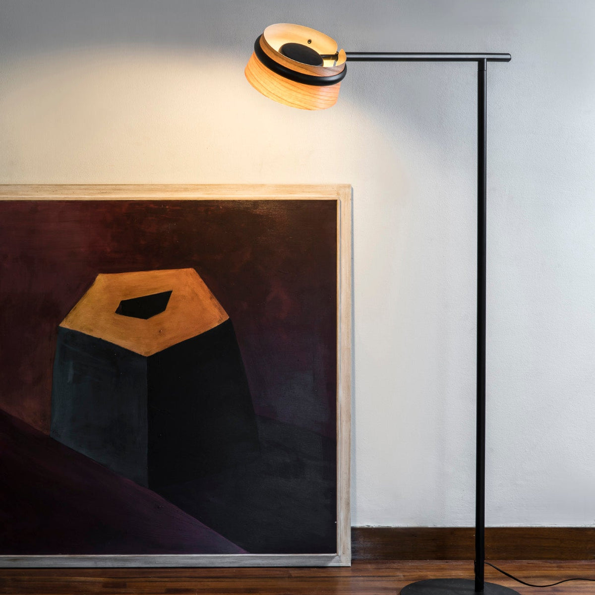 Modern floor lamp with a black base and gold shade next to a painting on a wall.