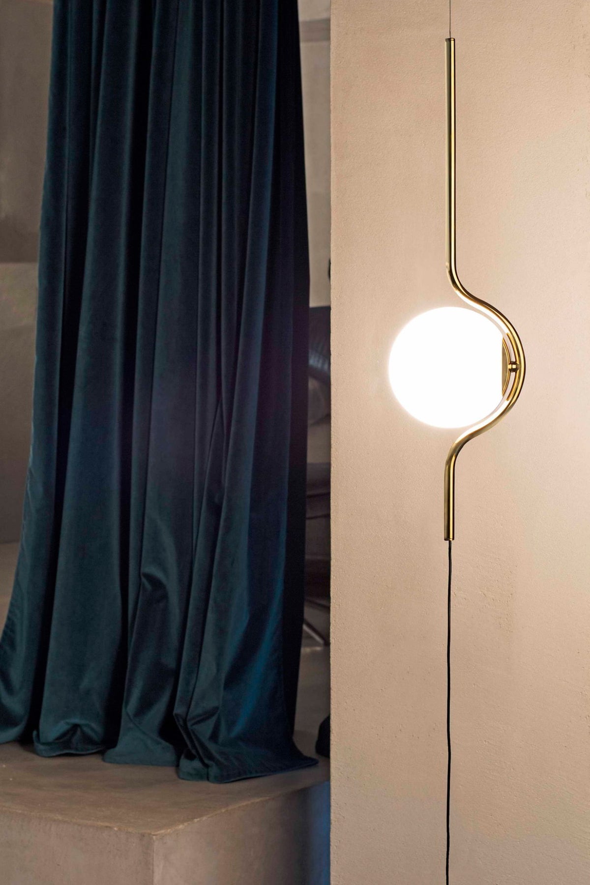 Modern floor lamp with a round glass shade next to a dark curtain.