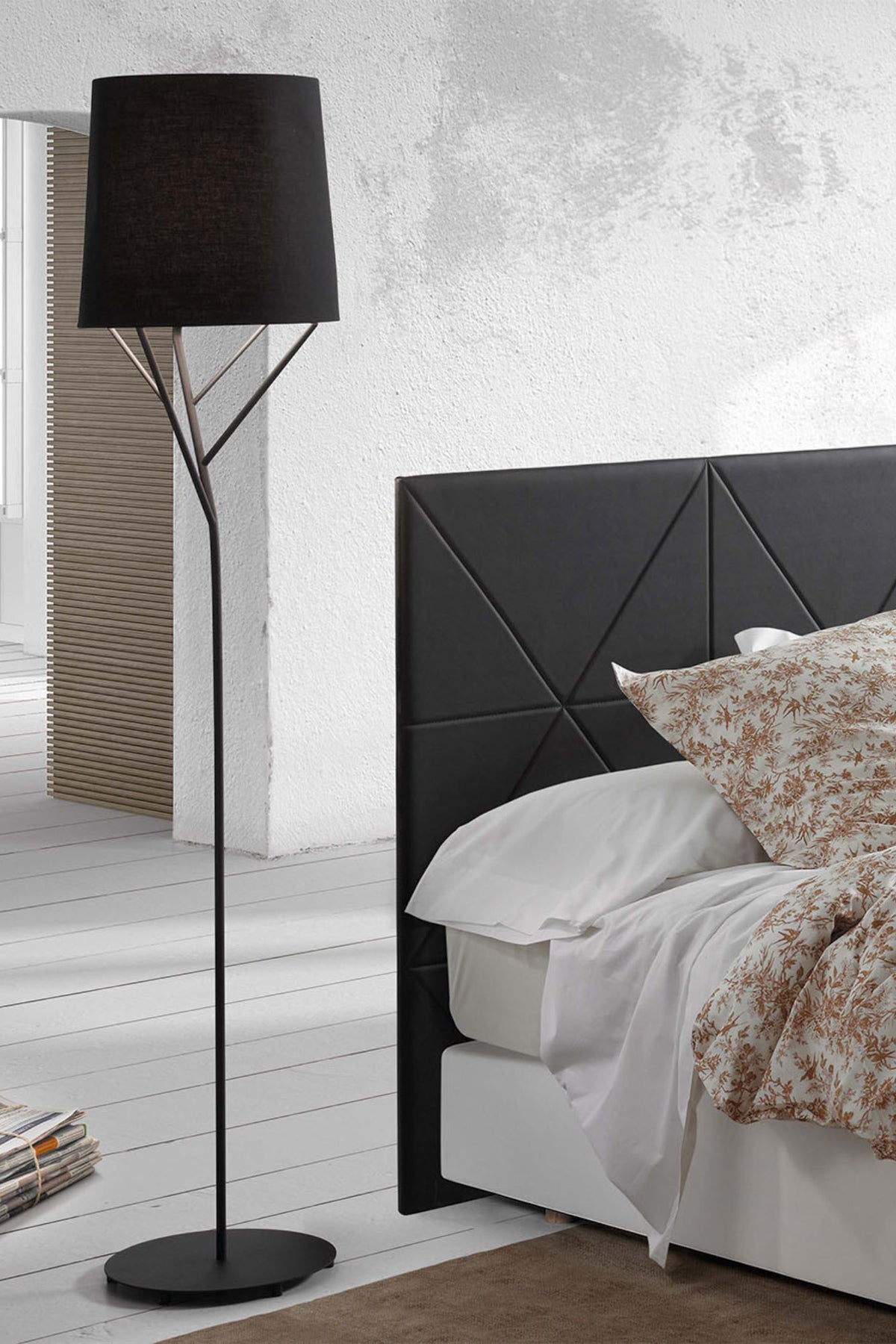 Modern bedroom with black geometric headboard, white bedding, and a black floor lamp.