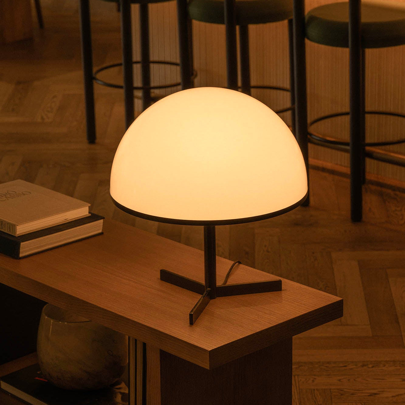 Table lamp on a wooden table with books and a vase in a dimly lit room.