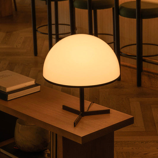 Table lamp on a wooden table with books and a vase in a dimly lit room.