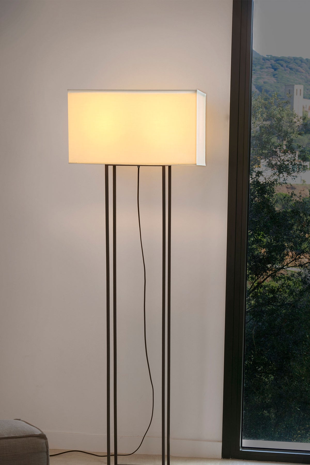 Floor lamp with a rectangular shade in a room with a window showing greenery outside.
