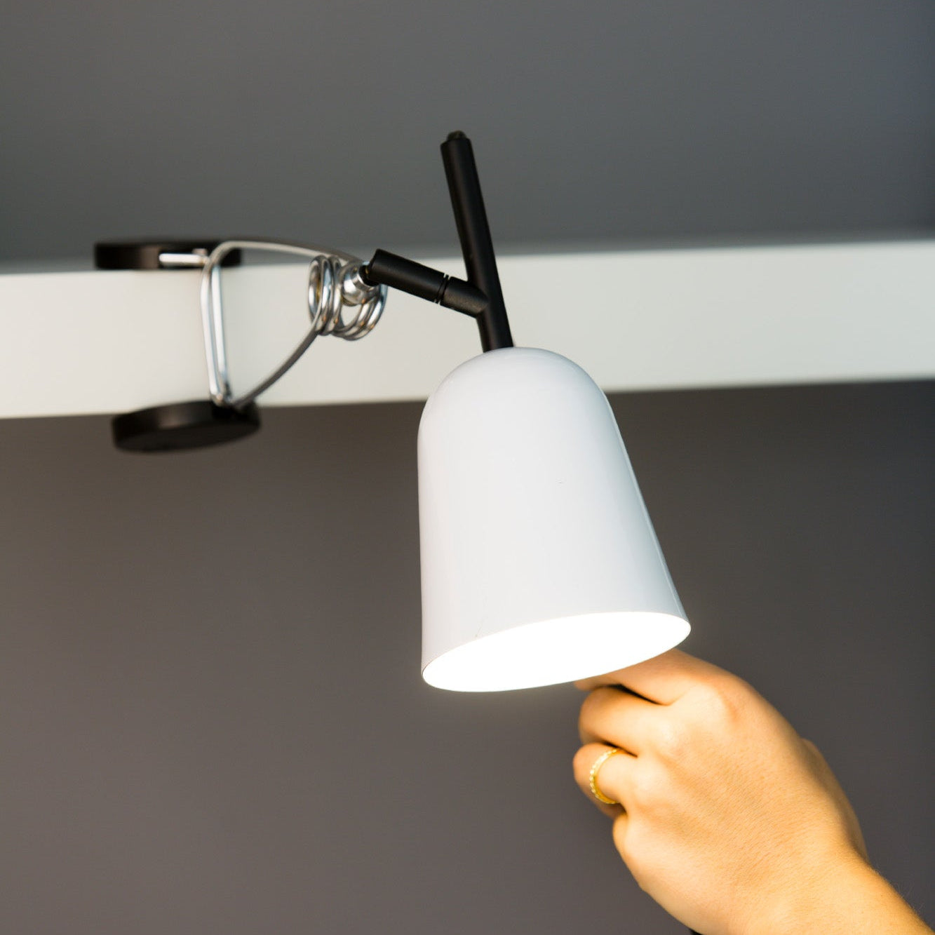Hand adjusting a white lampshade on a ceiling fixture against a gray background