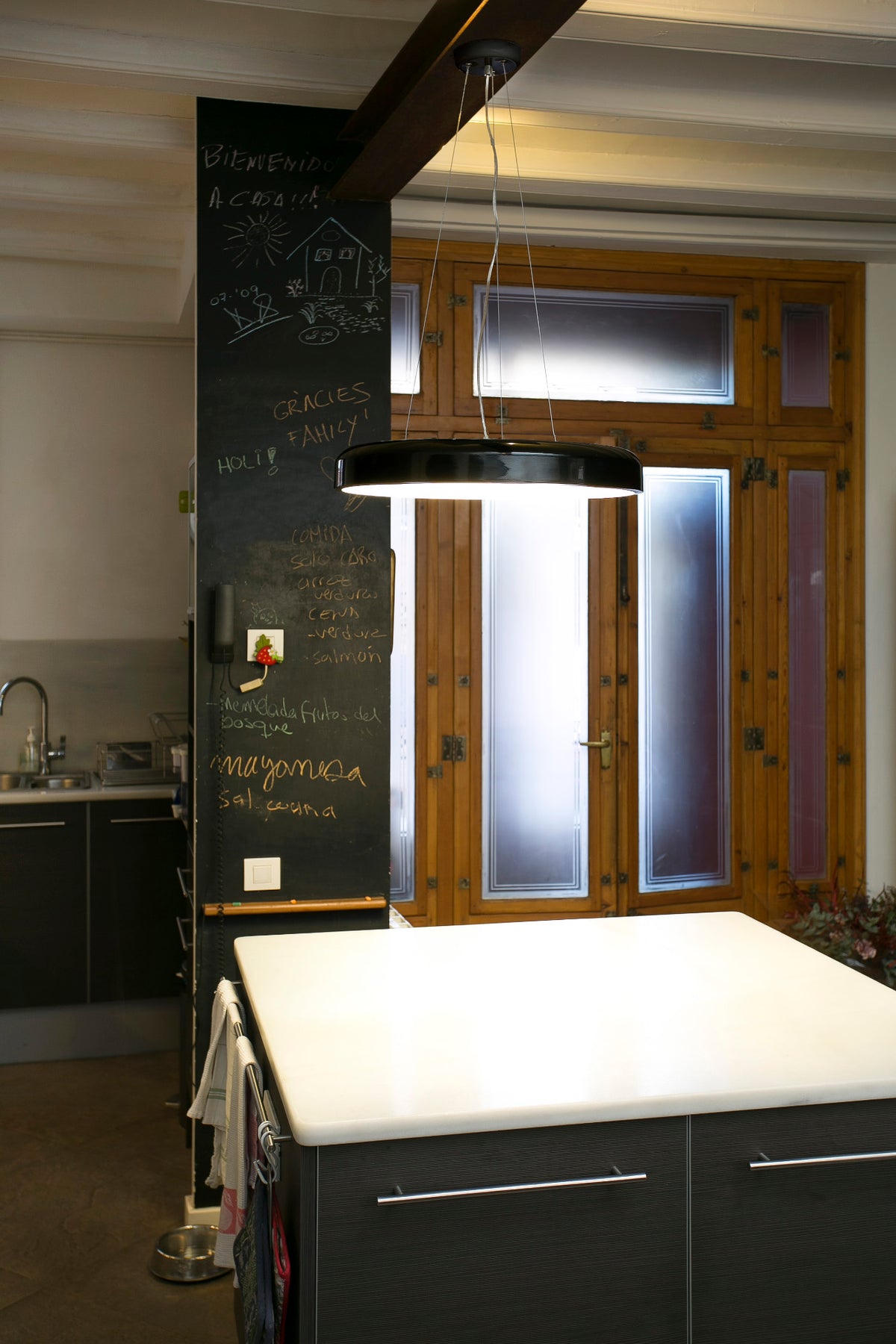 Modern kitchen with white countertop, blackboard wall, and large pendant lamp