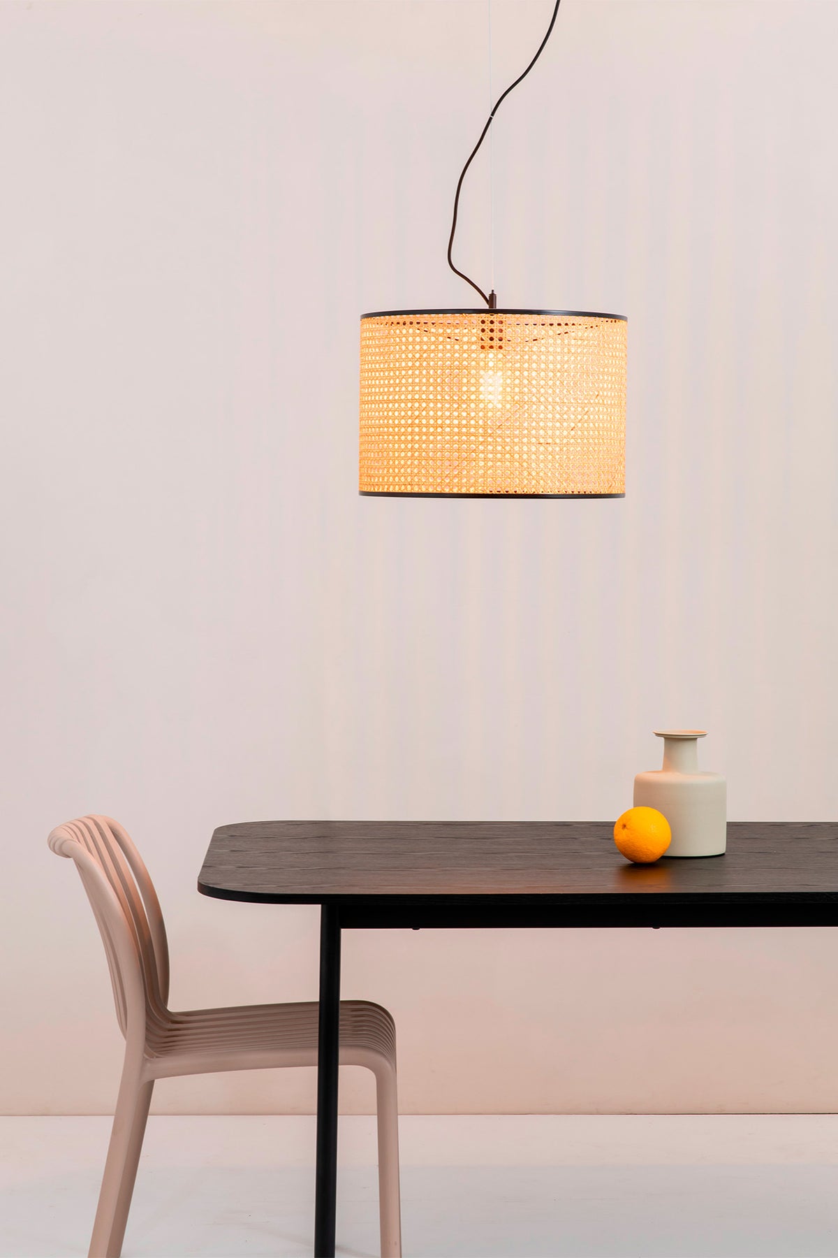 Modern dining setup with a black table, chair, and pendant light against a white wall.
