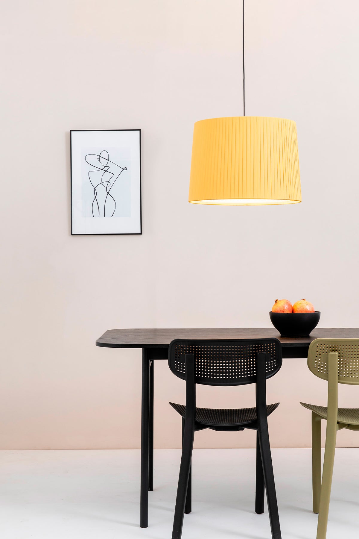 Dining area with a black table and chairs, yellow pendant lamp, and framed artwork on a light pink wall.