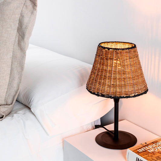 Wicker lamp on a nightstand next to a book with 'Interiors Nom' on a bed.