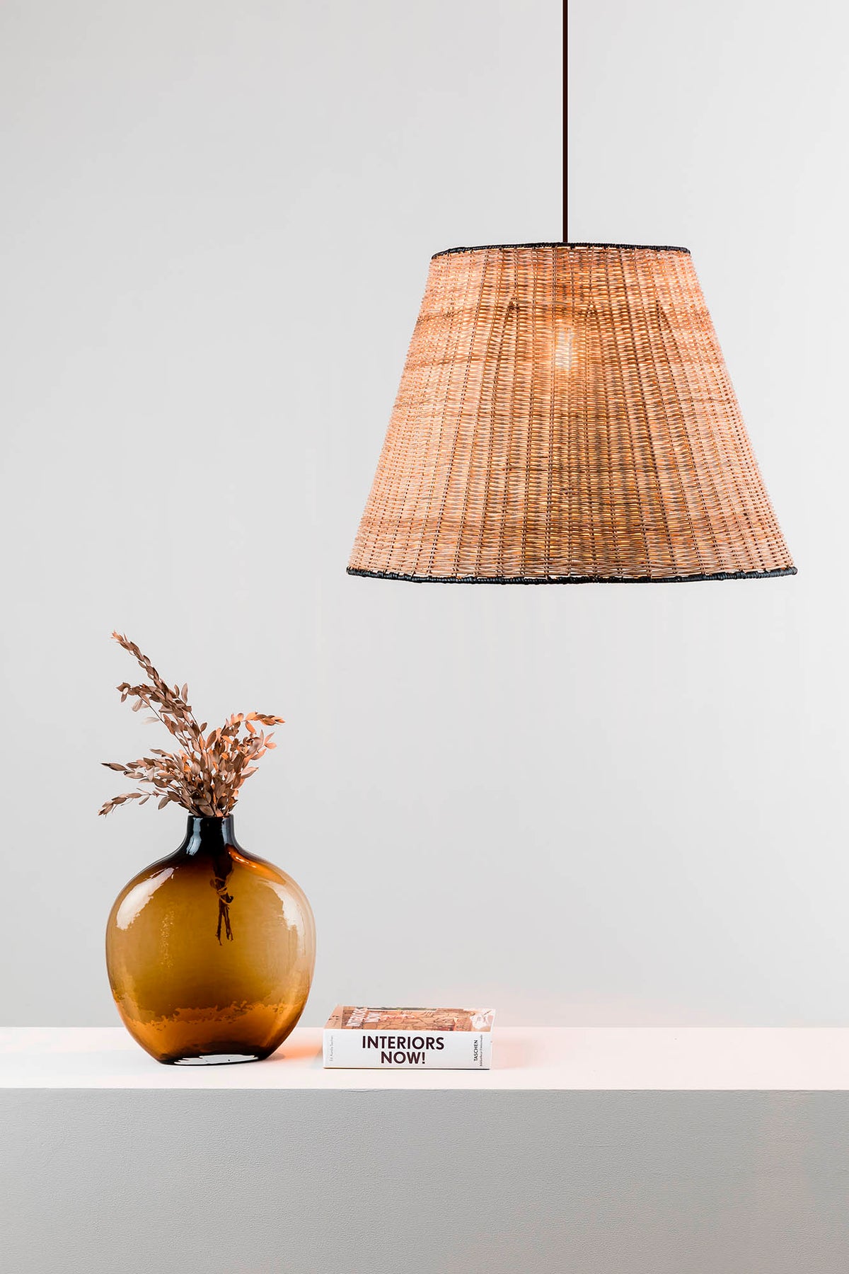 Wicker pendant lamp hanging above a table with a vase and book on a light gray background