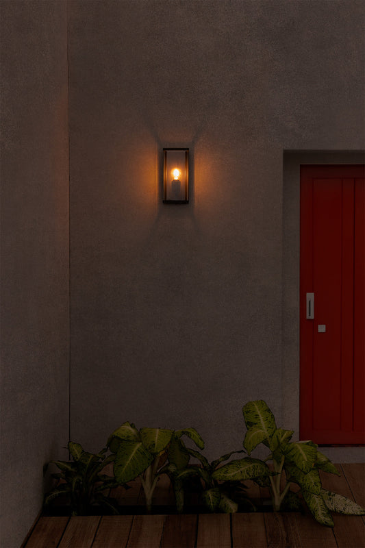 Wall-mounted light fixture on a textured wall with a red door in the background.