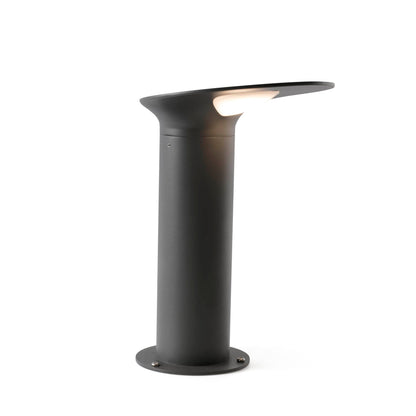 A modern outdoor bollard light with a matte black cylindrical base and a curved, shield-like top shade that glows with warm white light, shown against a solid white background.