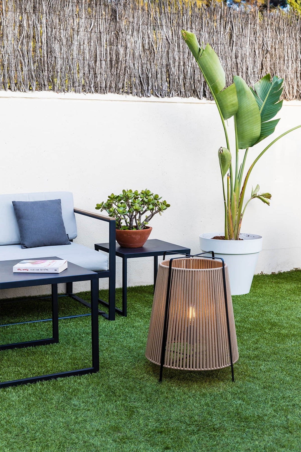 Outdoor patio setup with a sofa, coffee table, and potted plants outdoor lamps