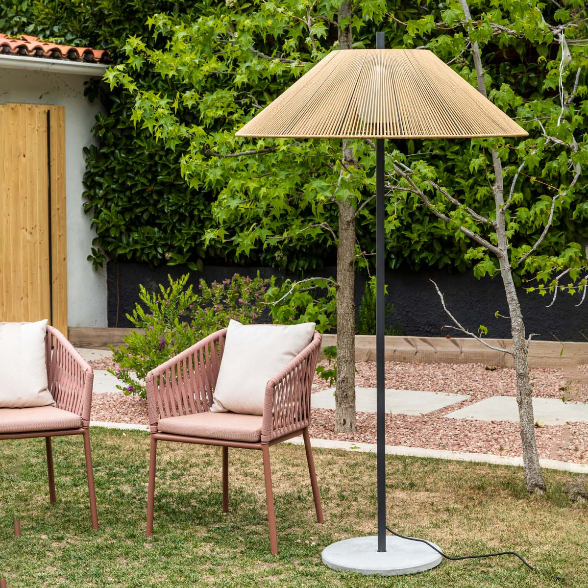 Garden scene with two pink chairs and a rattan umbrella in a backyard setting.