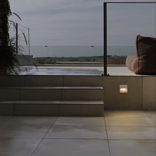 Outdoor patio area with steps leading to a pool or water feature, illuminated by wall lights.
