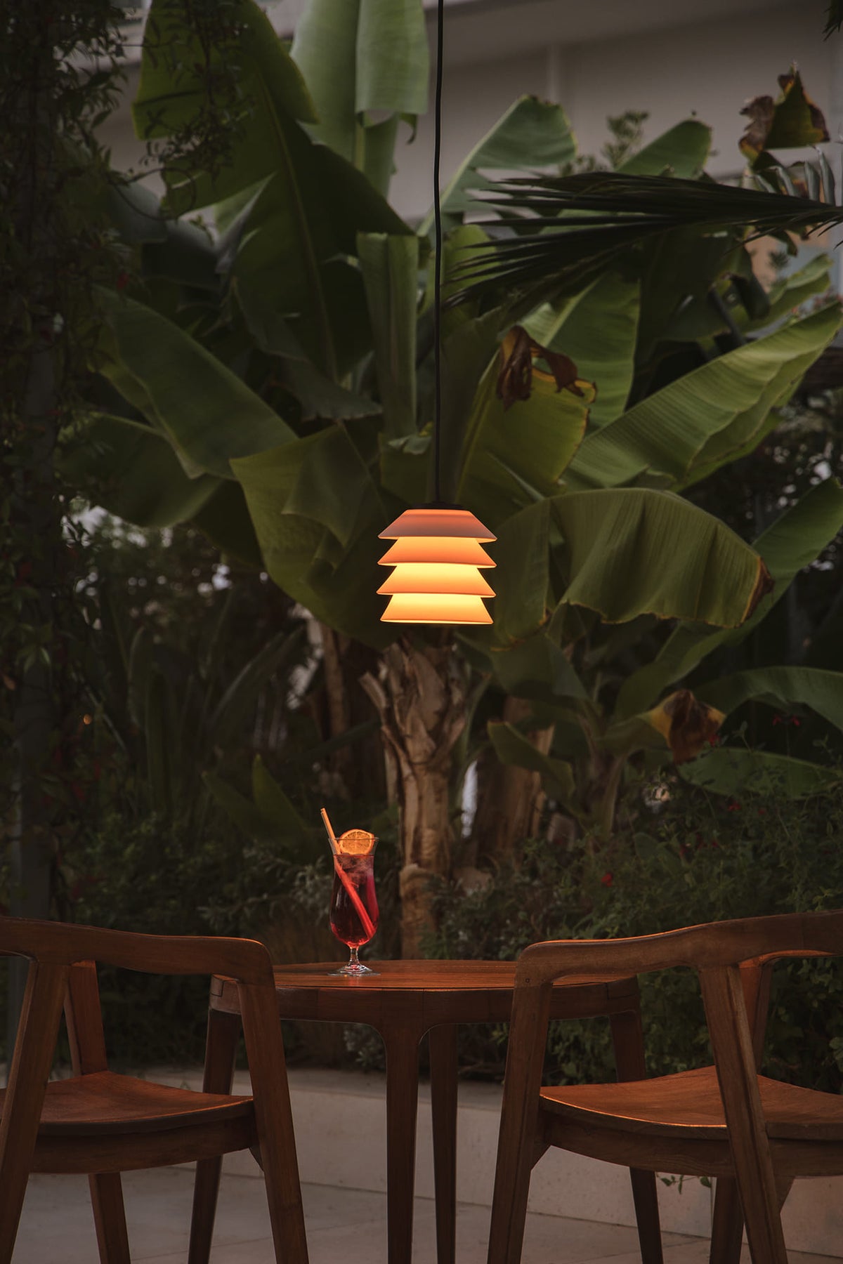 Tropical outdoor setting with a cocktail on a table under a hanging lamp.