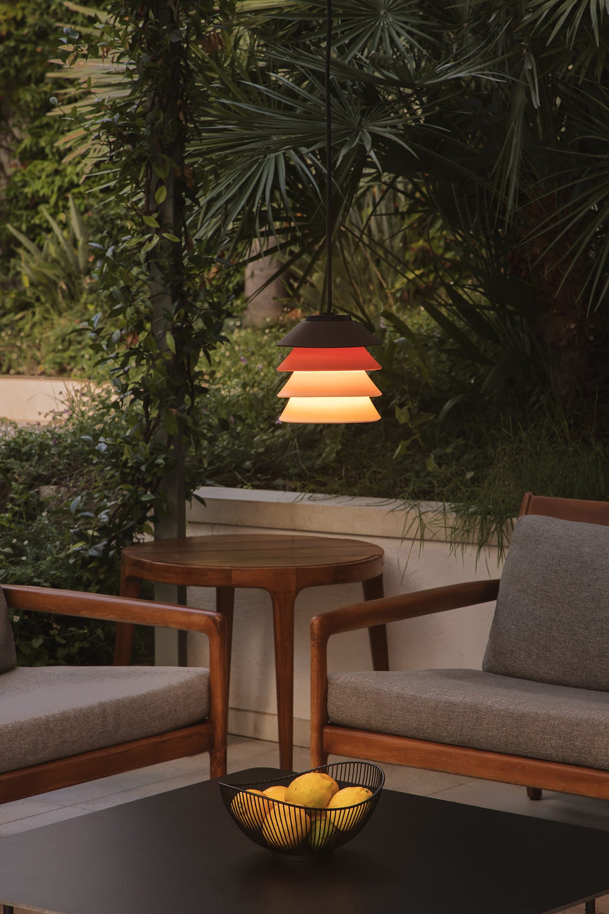 Outdoor setting with wooden furniture, a hanging lamp, and a bowl of fruit.