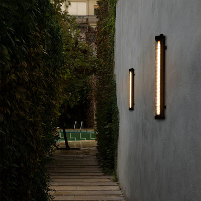 Pathway with outdoor wall lights on a gray wall, leading to a garden area.