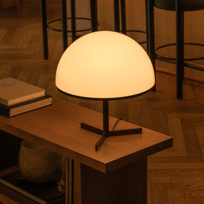 Table lamp on a wooden table with books and a vase in a dimly lit room.