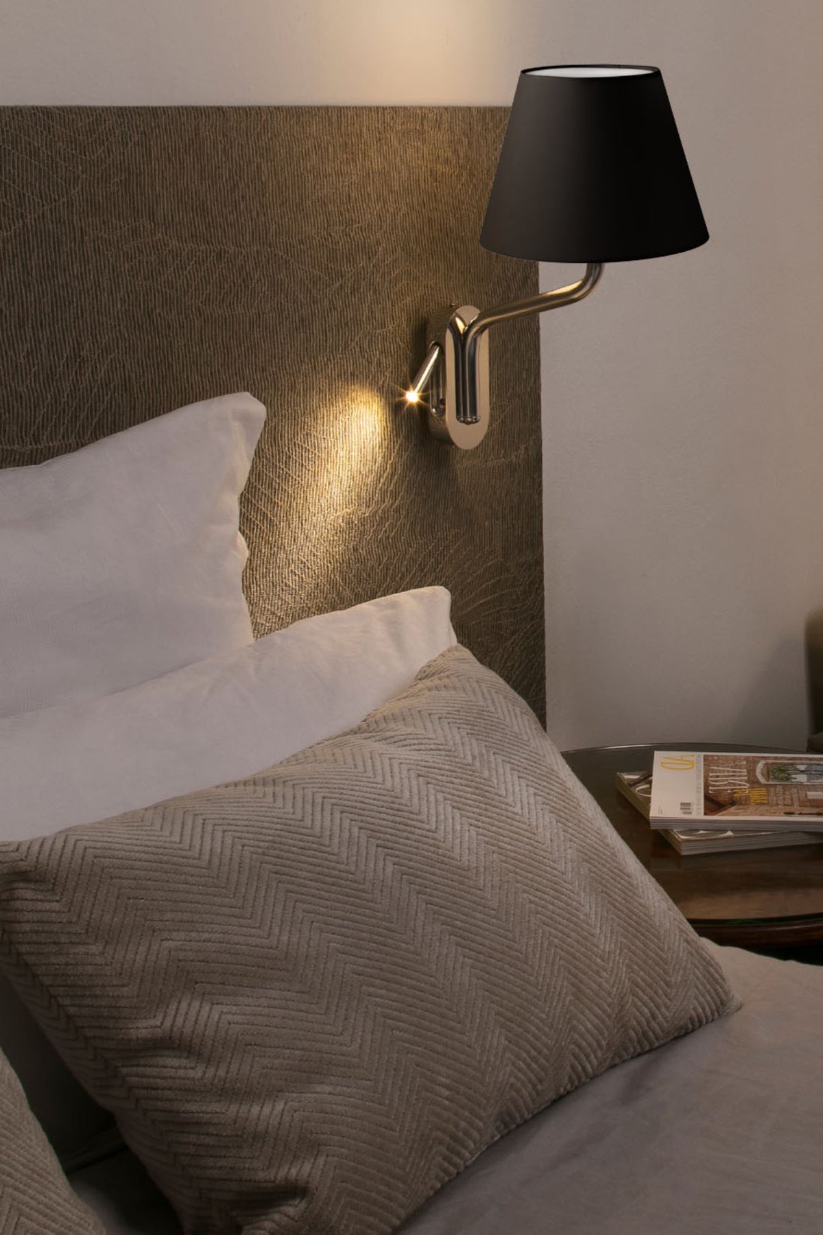 Bedroom scene with a wall-mounted lamp casting light on pillows and a nightstand.