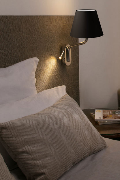 Bedroom scene with a wall-mounted lamp casting light on pillows and a nightstand.
