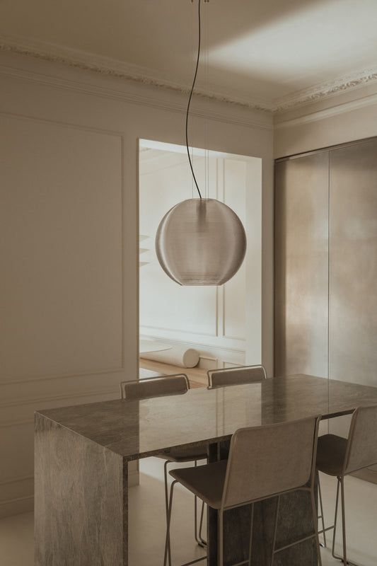 The Aire 650 translucent pendant light by Faro Barcelona suspended above a modern marble dining table in an elegant interior. Showcases sustainable 3D-printed PETG design, available at the VXR Space store.