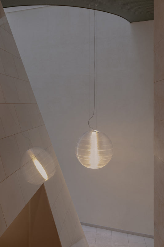 The AIRE 850 oversized pendant light by Faro Barcelona suspended in a modern, light-filled architectural interior. The glowing spherical fixture creates a dramatic focal point, available to buy at the VXR Space store.