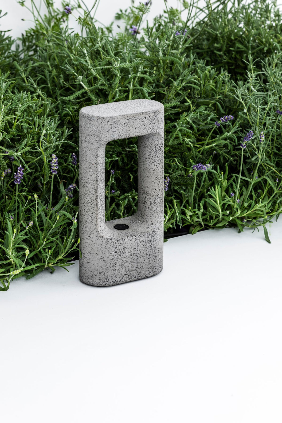The Totem 285 grey cement outdoor LED bollard lamp by Roger Vancells integrated among garden plants and lavender, presented by the VXR Space store.