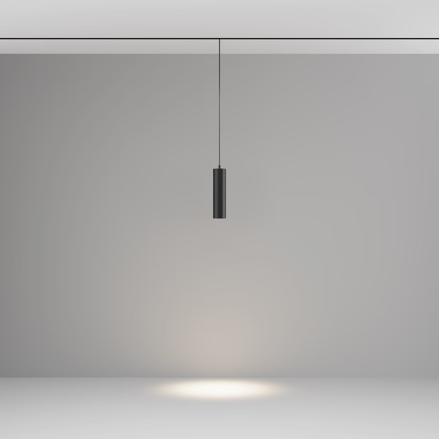 A modern black cylindrical track pendant light hanging from a thin cord against a minimalist gray studio background, casting a warm spotlight downward on the floor.