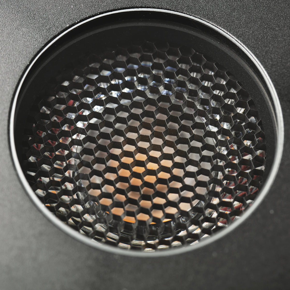 Close-up of a circular black honeycomb-patterned speaker grille or vent on a dark gray surface.