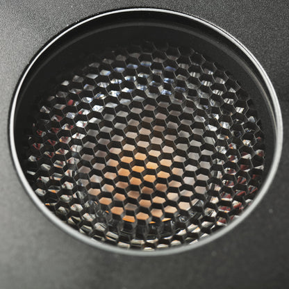 Close-up of a circular black honeycomb-patterned speaker grille or vent on a dark gray surface.