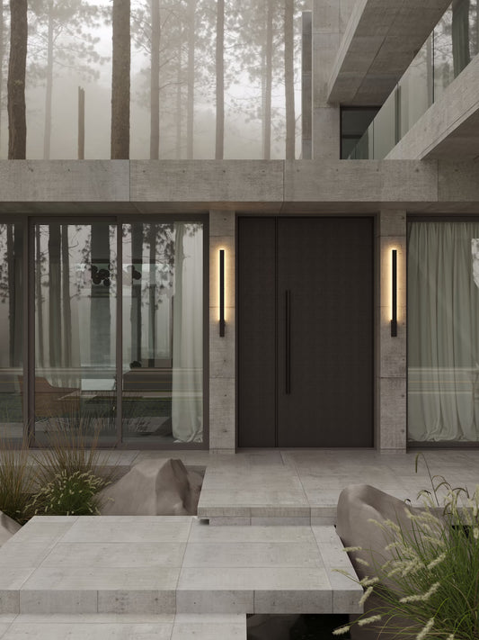 The Kaprun black modern LED outdoor wall lights installed vertically on a concrete exterior wall beside a dark entrance door. Available to buy at the VXR Space store.