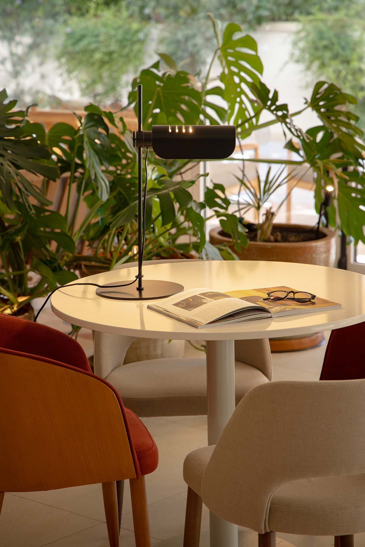 Round table with a lamp, book, and glasses in a room with plants