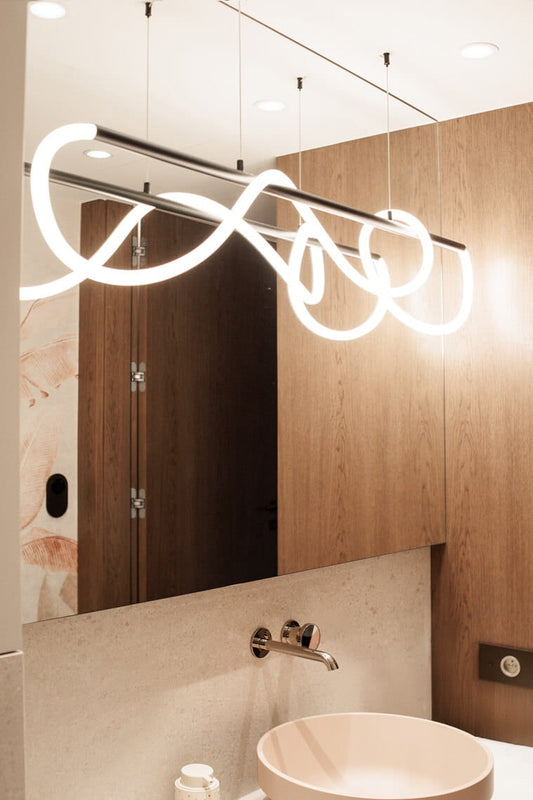 The Laguna 1200mm modern curved LED pendant light by MaxLight installed above a modern sink and mirror in a luxury bathroom interior. Available to buy at the VXR Space store.