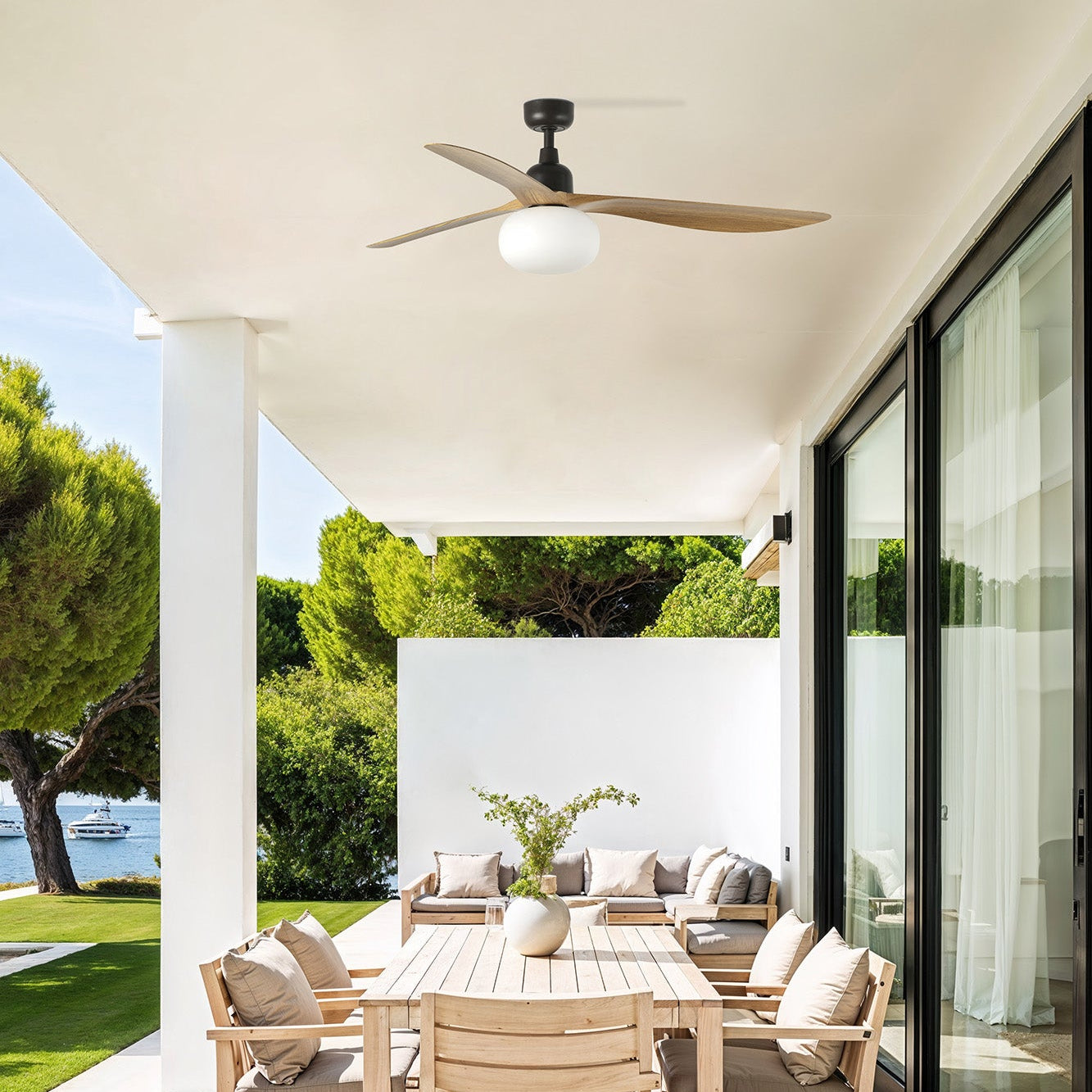 Modern outdoor patio with wooden furniture, ceiling fan, and view of trees and water.