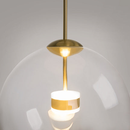 A modern pendant light with a large clear glass globe shade, a polished brass suspension rod and canopy, and a glowing white cylindrical bulb holder in the center, shown against a neutral gray background.