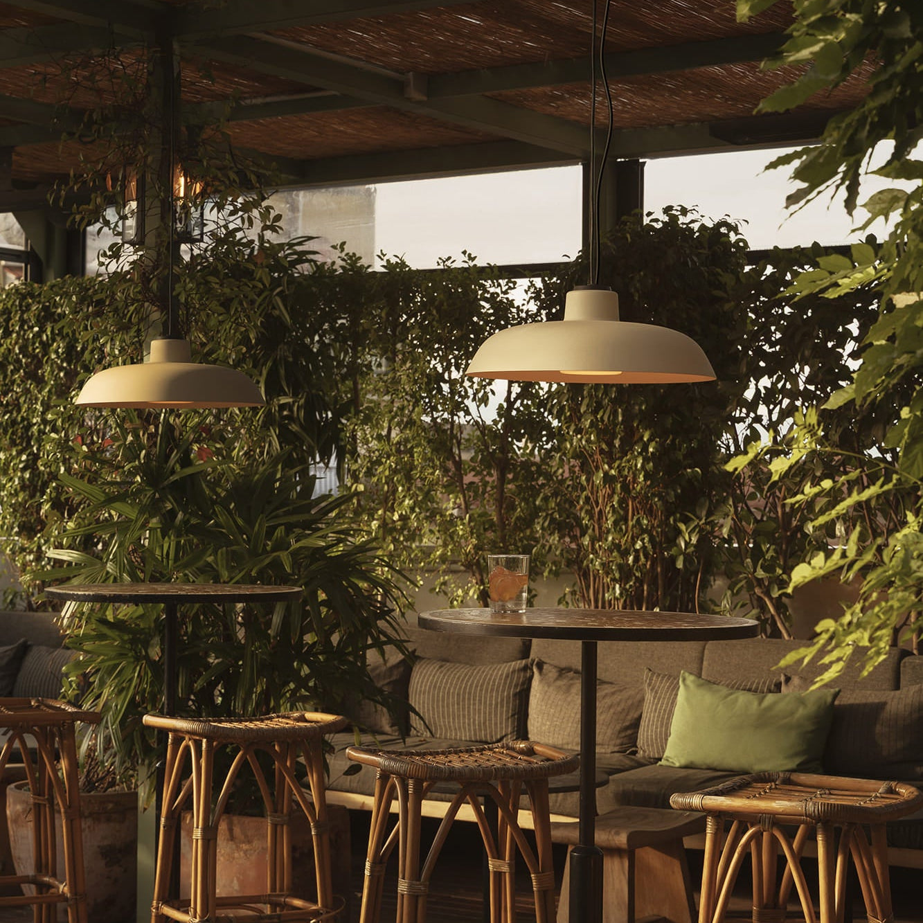 Outdoor patio with wooden tables, stools, and hanging lights surrounded by greenery.