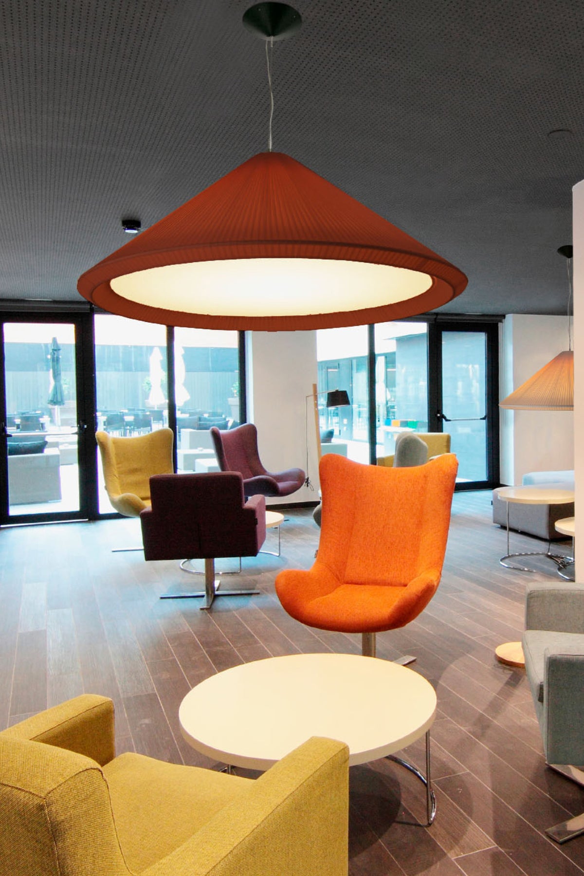 Modern office lounge with colorful chairs and a large pendant light.