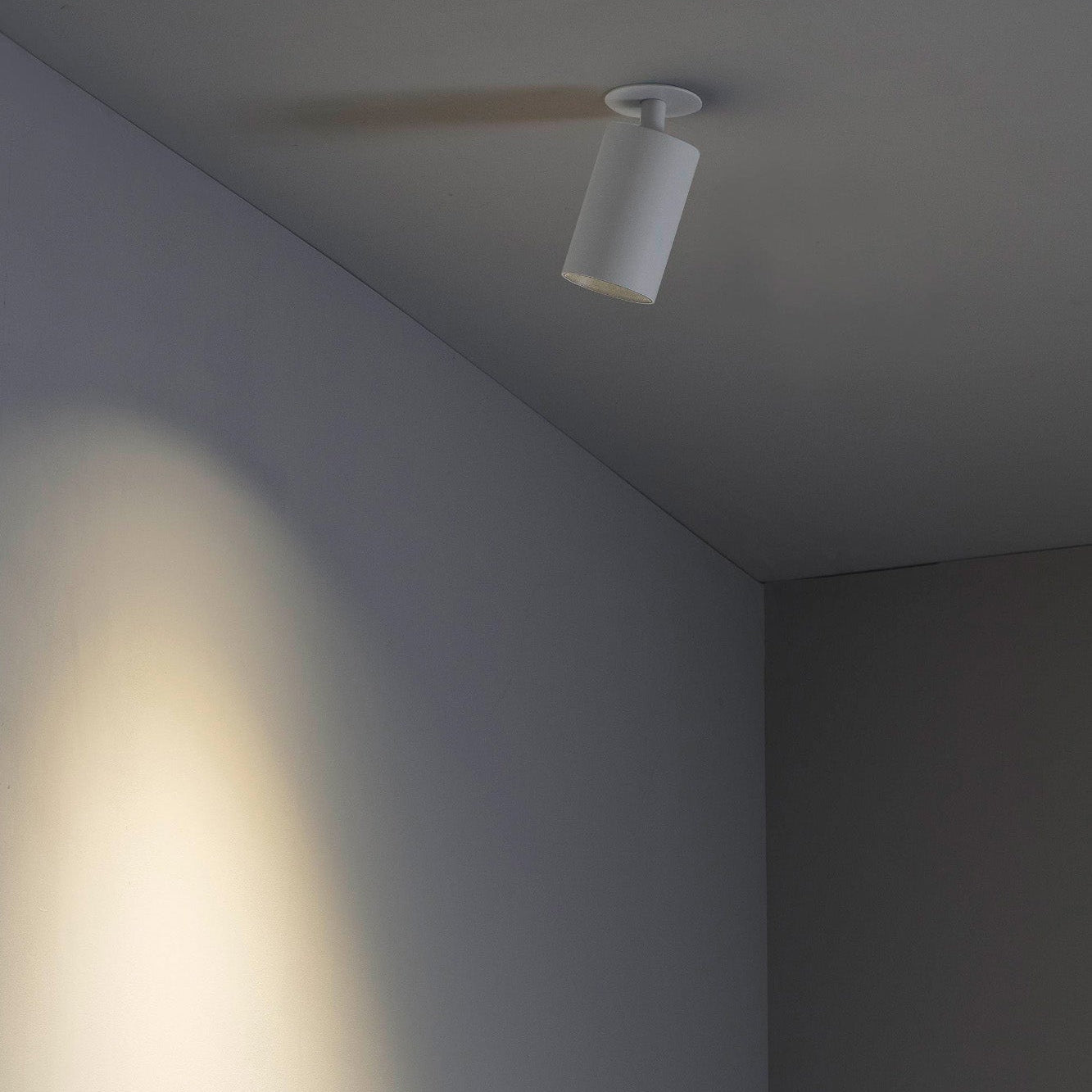 Ceiling light fixture casting a shadow on a wall in a minimalistic room.
